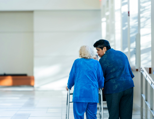 An older woman with a walker and a younger woman walking next to her in a hallway.
