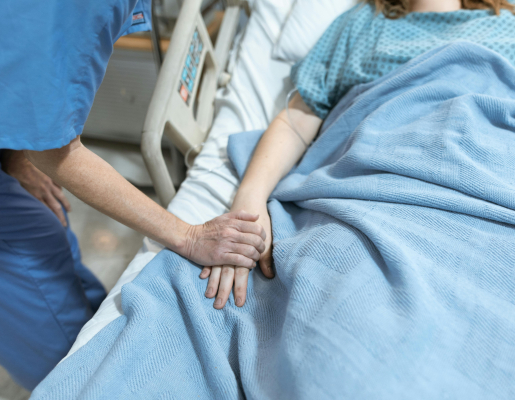 Image of a patient in a bed and a nurse holding their hand.