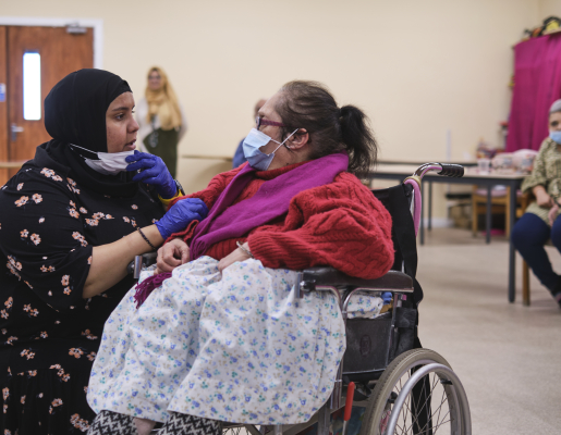 Younger woman wearing a hijab and kneeling, talking to an older woman in a wheelchair.