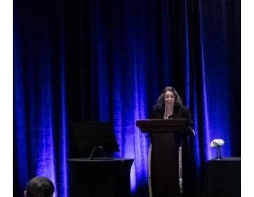 Alison on stage at the podium presenting a slideshow.