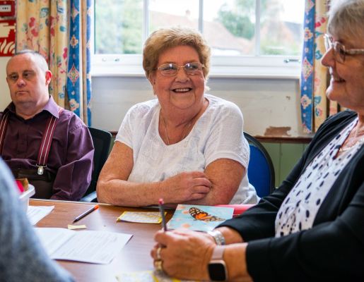 Group of older adults sitting around a table smiling and having conversation.