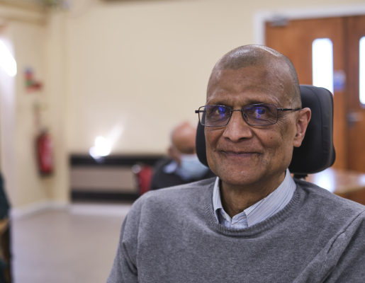 Image of a brown man wearing glasses, sitting in a motorized wheelchair.