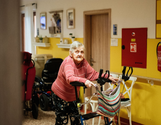 An older adult using a walker in the hallway of a nursing home. 