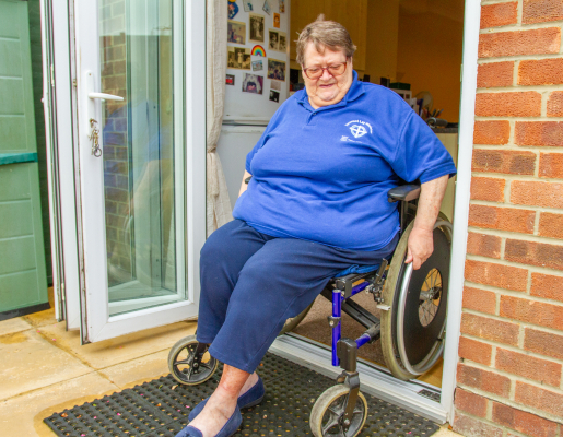 A Wheelchair user in their chair, wearing a blue shirt and jeans, in the doorway.