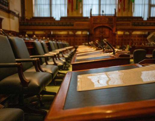 A row of desks in a legislative chamber, with a chair and microphone by every desk.
