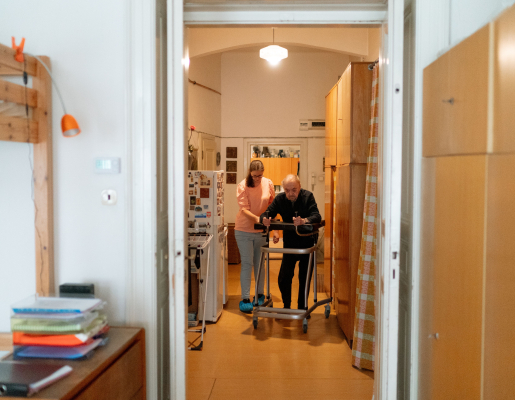 View through a doorway of a younger adult helping an older adult with a walker.