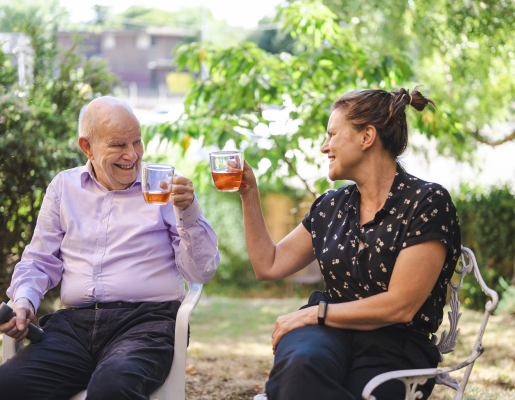 Image of a younger woman and older man sitting outside, smiling and holding mugs.