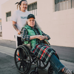 Older adult being pushed in a wheelchair by a younger adult.