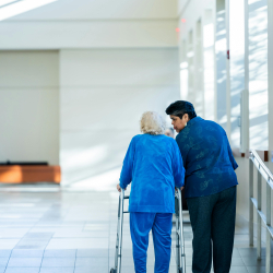 An older woman with a walker and a younger woman walking next to her in a hallway.