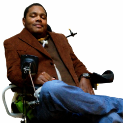 Photo of Travar Pettway sitting in a motorized wheelchair wearing a brown suit jacket and jeans.