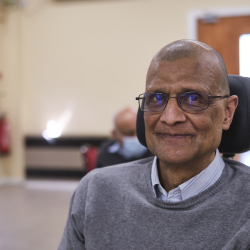 Image of a brown man wearing glasses, sitting in a motorized wheelchair.
