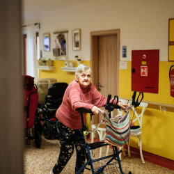 An older adult using a walker in the hallway of a nursing home. 