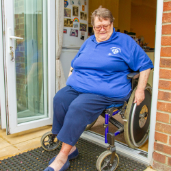 A Wheelchair user in their chair, wearing a blue shirt and jeans, in the doorway.