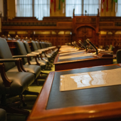A row of desks in a legislative chamber, with a chair and microphone by every desk.