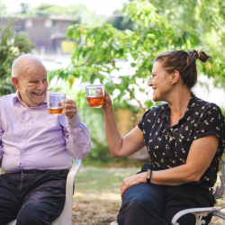 Image of a younger woman and older man sitting outside, smiling and holding mugs.